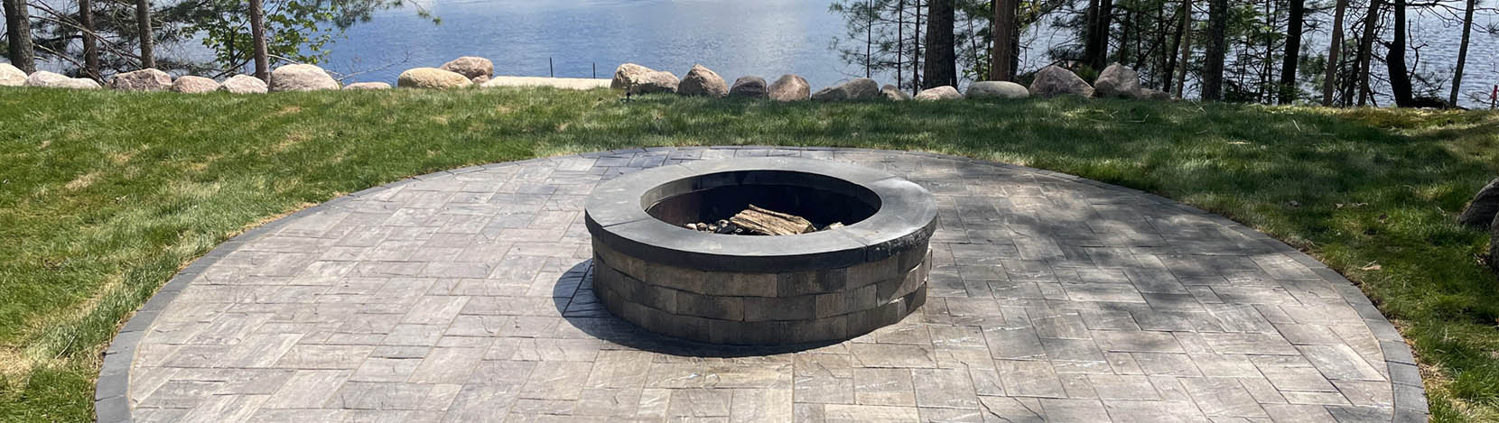 Northern Dreamscape patio with a fire pit on a beautiful Wisconsin property overlooking a rock wall to views of the lake.